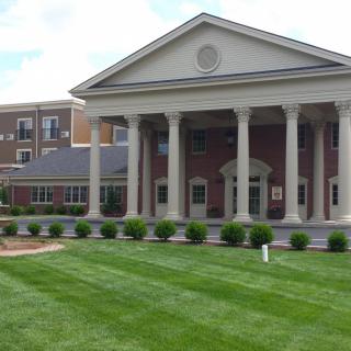 A classical-style brick building with columns and a well-maintained lawn.