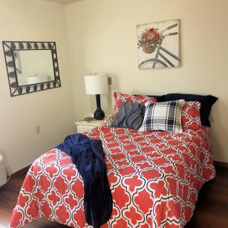 A cozy bedroom with bright red patterned bedding, stylish pillows, and a decorative wall mirror.