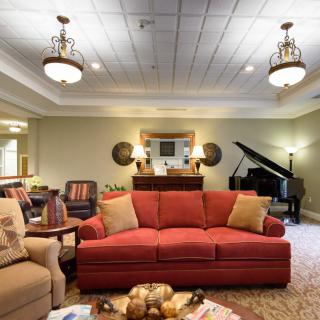 A cozy living room with a red sofa, piano, and elegant chandeliers.