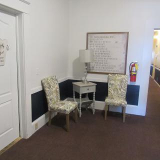 A cozy hallway corner with patterned chairs, a side table, and a lamp.