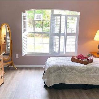 A cozy bedroom with a large window, featuring a bed, dresser, and lamp.