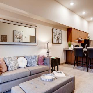 A stylish and cozy living room with a sofa, large mirror, and artwork, leading into a kitchen area with bar stools.