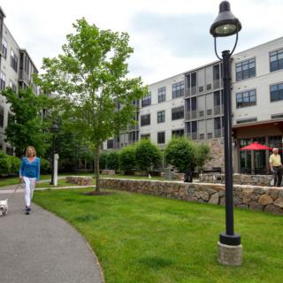 A person walks along a path in a well-maintained outdoor area of an apartment complex.