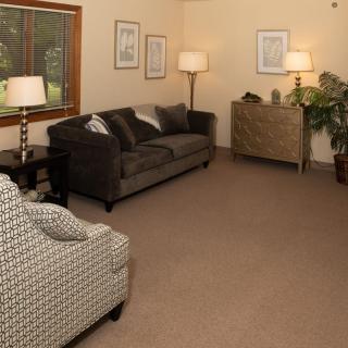 A cozy living room with a comfortable sofa and armchair, illuminated by soft lighting and decorated with plants and artwork.