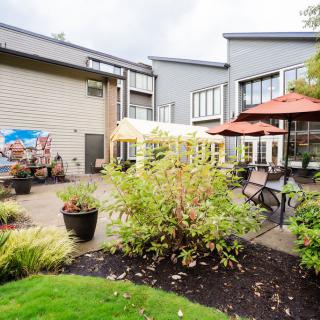 A well-maintained outdoor patio and garden area with seating, umbrellas, and landscaping outside a modern building.