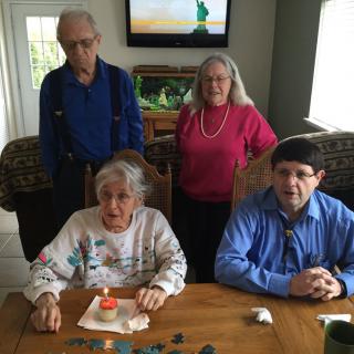 A family gathering with four people posing together indoors, two seated at a table and two standing behind them.