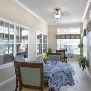A bright and airy dining area with windows, featuring tables covered with floral tablecloths and surrounded by chairs.