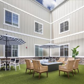 A cozy outdoor patio area with seating and umbrellas, surrounded by a building with multiple windows.