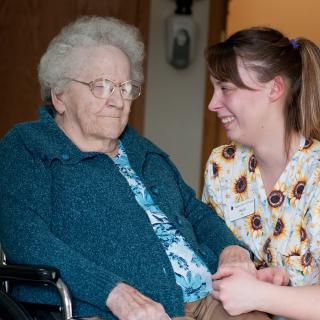 A nurse interacts warmly with an elderly woman in a wheelchair.