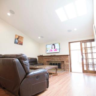 A spacious living room with a leather sofa, fireplace, and a wall-mounted TV. The room is brightened by a skylight and features wooden flooring.