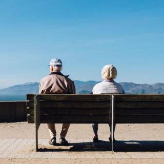 An elderly couple enjoys a peaceful moment by the seaside on a sunny day.