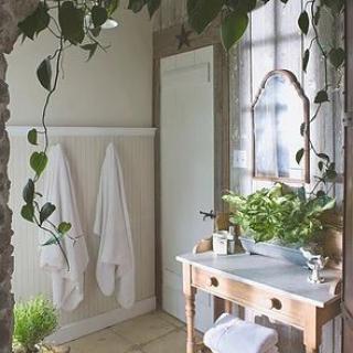 A bright bathroom with plants, a wooden sink stand, and white towels hanging on the wall.