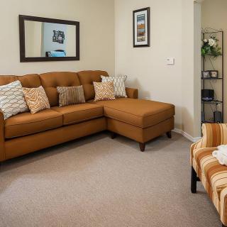 A cozy living room featuring a brown sectional sofa with patterned cushions, a mirror on the wall, and a comfortable chair.