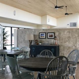 A modern dining area featuring wooden tables and chairs, complemented by a stone wall and abundant natural light.