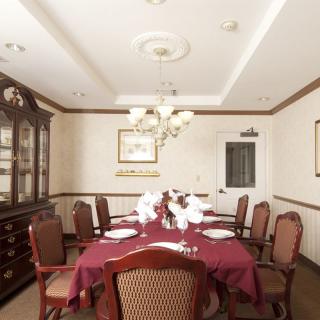An elegant dining room with a large table, surrounded by chairs and illuminated by a chandelier.