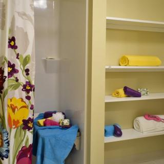 A bathroom with a floral shower curtain and neatly arranged towels on open shelves.