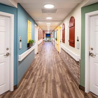 A brightly colored corridor with wooden flooring and variously colored doors and decorative windows.