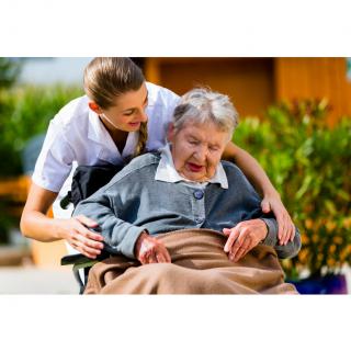 A caregiver assisting an elderly person in a wheelchair outdoors.