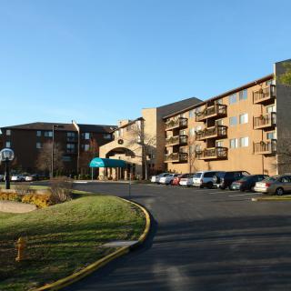 A four-story hotel building with a parking lot in front, under a clear blue sky.
