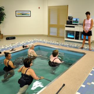 A water aerobics class taking place in an indoor pool with an instructor leading a group of participants.
