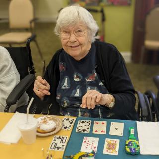 An elderly woman smiling while playing a game of cards at a table indoors.