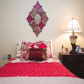 A cozy bedroom with red bedding and a bedside lamp, featuring decorative wall art.
