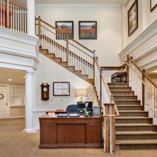 A welcoming lobby area featuring a wooden reception desk and a grand staircase with decorative railings.