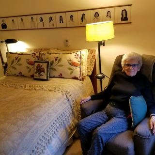 A cozy bedroom with a woman sitting in an armchair next to a well-made bed.