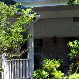 A cozy house with a porch surrounded by lush greenery and trees.