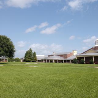 A serene view of a school campus featuring well-maintained buildings and lush green grass under a clear blue sky.