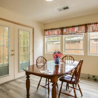 A bright dining room featuring a wooden table set with chairs and decorated with a vase, illuminated by natural light from windows and French doors.
