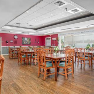 An empty dining room with wooden tables and chairs, featuring bright lighting and decorative paintings on the walls.