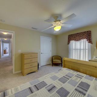 A cozy bedroom with a bed, dresser, ceiling fan, and window.