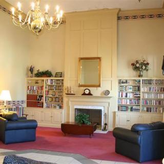 A traditional living room with a central fireplace, bookshelves, and comfortable armchairs, illuminated by a chandelier.