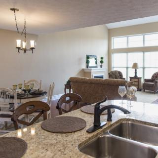 An open-concept living space featuring a kitchen with granite countertops and a sink, adjacent to a dining area, and a cozy living room with large windows.