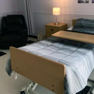 A tidy hospital room with a bed, lamp, and chair.