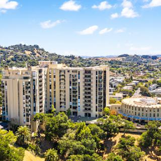 A view of a modern residential building set against a backdrop of lush greenery and hills.