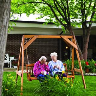 An elderly couple sitting together on a wooden swing in a lush garden.