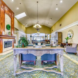 A spacious living room with elegant decor, featuring a central table and chairs, chandelier lighting, and a fireplace.