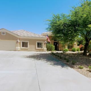 A charming single-story house with a spacious driveway and well-maintained front yard under a clear blue sky.