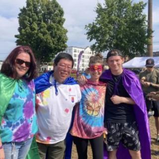 A group of people wearing colorful tie-dye shirts and capes at an outdoor event.