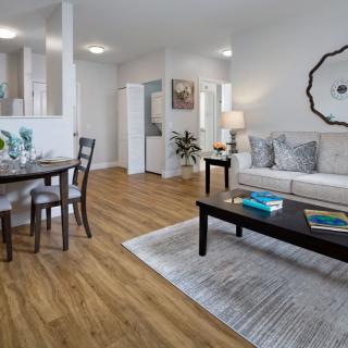 A modern living room with wood flooring, featuring a sofa, coffee table, and dining area.