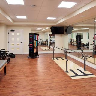 A spacious gym with wooden floors, mirrors, and fitness equipment including a ballet barre.