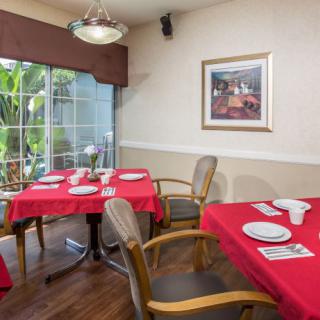 An inviting dining area with red tablecloths, neatly set tables, and a garden view through large windows.