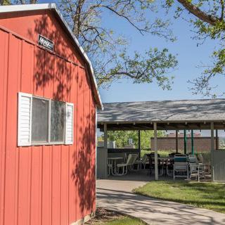 A sunny outdoor scene featuring a red building with a nearby shaded patio area.