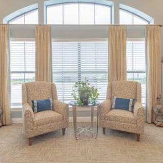 A cozy living room setup featuring two armchairs and a small glass coffee table in front of large windows with curtains.