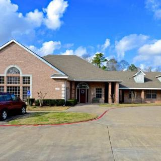 A residential style building with a car parked in the driveway under a blue sky with clouds.