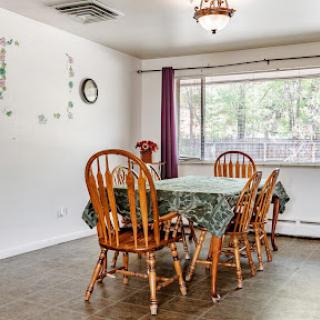 A cozy dining room featuring a wooden table surrounded by chairs, brightened by natural light from the nearby window.