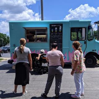 A group of people waiting in line at a colorful food truck on a sunny day.