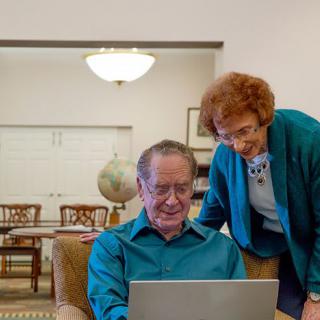 An elderly couple enjoying time together while using a laptop in their living room.